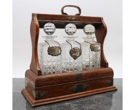 An oak three bottle tantalus,with three cut glass bottles, two with silver spirit labels for 'Whisky' and 'Sherry', by Crisfo