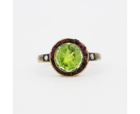 An antique rose metal (tests 9ct gold) ring set with a large round peridot surrounded by rubies (some A/F) and diamond set sh