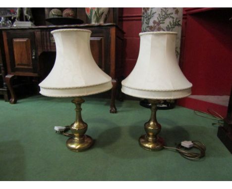 A pair of brassed table lamp bases with cream shades
