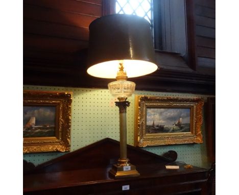 A brass columnar oil lamp, converted to an electric table lamp, having clear glass reservoir over Corinthian column on a step