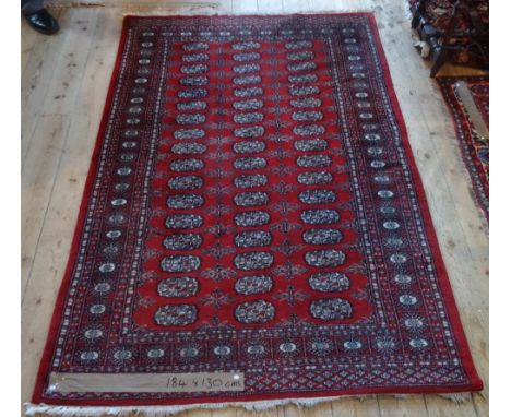 A man made Bokhara-style carpet, with repeating geometric shapes on a deep red ground (184cm x 130cm).