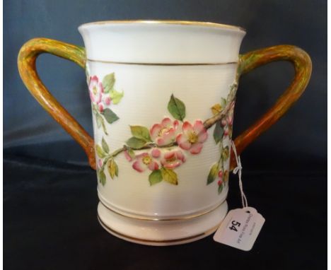 A large Royal Worcester loving cup, having pink blossom decoration in shallow relief, the twin handles formed as stylized bra