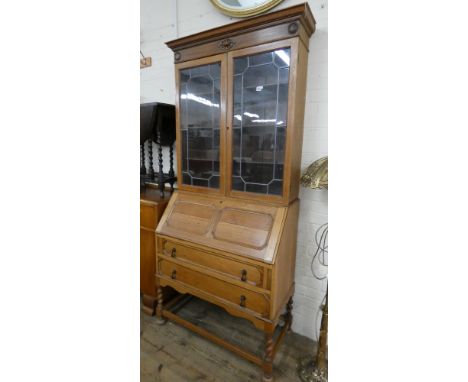 A light oak 1930's bureau bookcase with leaded glazed doors, fall flap and two drawers under on barley twist legs 