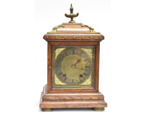 AN EDWARDIAN 8-DAY MANTLE CLOCK  the silvered dial with Roman numberals and brass cherub spandrels, in a brassmounted oak cas