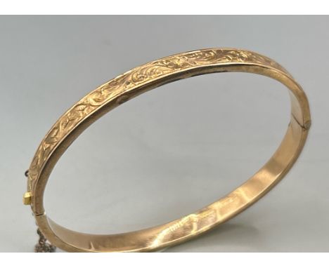 A yellow gold hinged bangle with engraved top decoration and safety chain, hallmarked 9ct 1974, gross weight 5.6g. / SF