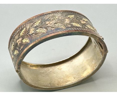 A hinged silver bangle with applied yellow and pink metal decoration to top, stamped sterling, gross weight 30.7g. / SF