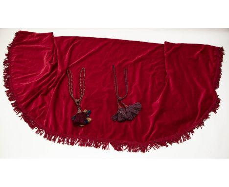 A large red velvet table cloth with large rope fringing. A pair of rope tie backs with tassels in a mix of red, navy and gold