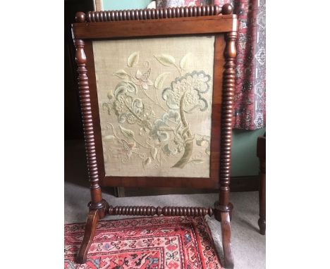 An early 19th Century mahogany firescreen, raised on bobbin turned supports, the panel embroidered with a foliage pattern, ra