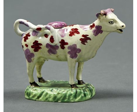 A LUSTRE WARE COW CREAMER AND COVER, MID 19TH C, SPONGED IN PURPLE LUSTRE AND RUST ENAMEL, ON GREEN MOUND, 14CM H Horns, ears