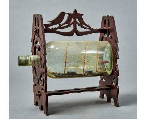 A VINTAGE SHIP IN A BOTTLE, THREE MASTED SCHOONER CONTAINED WITHIN A BOTTLE WITHIN A FRET CUT FRAME, THE ENDS AND HANDLE AS P