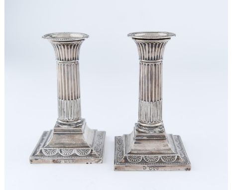 A PAIR OF VICTORIAN SILVER DWARF COLUMNAR SILVER CANDLESTICKS, THE BEADED SQUARE CAVETTO FOOT EMBOSSED WITH PATERAE, NOZZLES,