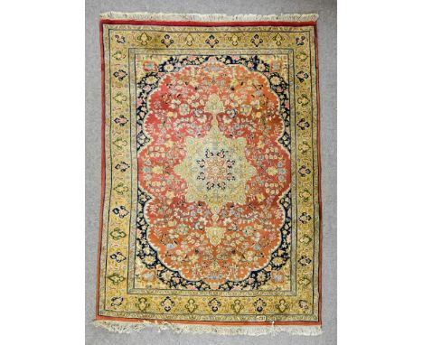 A 20th Century Kashan Carpet, woven in colours of green, fawn, navy blue and wine, with a bold central stylised floral medall