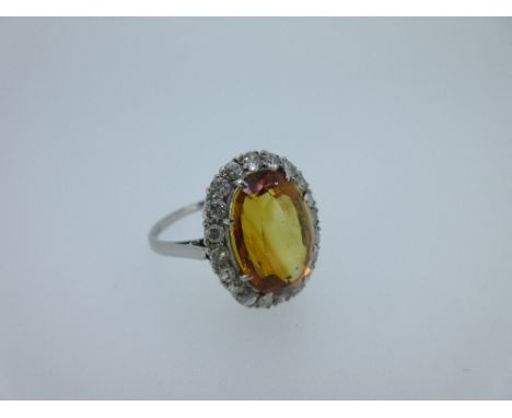 A citrine and diamond cluster ring, the oval cut citrine claw set to a border of round brilliant cut diamonds, to a pierced c