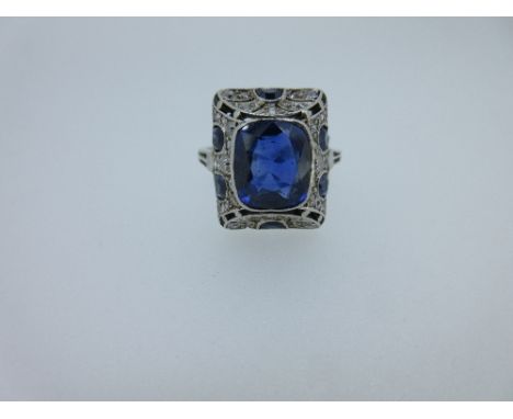 An Art Deco sapphire and diamond ring, the rectangular cushion cut sapphire collet set to a raised pierced surround, the ends