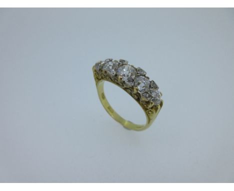 An 18ct gold five stone diamond ring, the five graduated old cut diamonds, spaced by diamond sparks to a carved scrolling gal