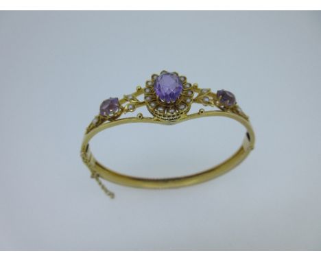 An amethyst and seed pearl set hinged bangle, with three knife edged bars flaring at the front and holding a central claw set