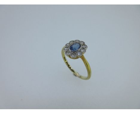 A sapphire and diamond oval cluster ring, the oval cut light-mid blue sapphire in a millegrain collet, to a petal edge border