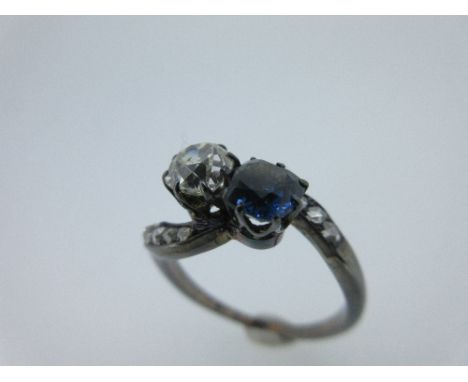 A sapphire and diamond two stone crossover ring, the old cushion cut diamond claw set obliquely to a similarly cut sapphire, 