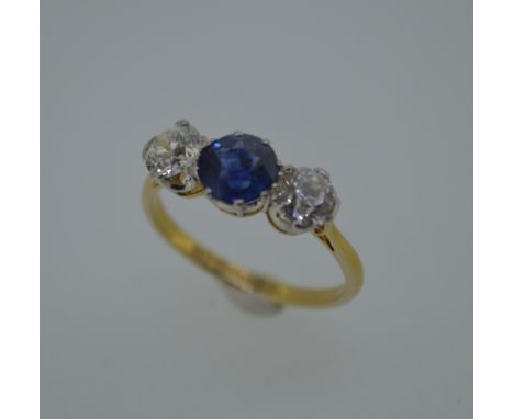 A diamond and sapphire three stone ring, the round cut sapphire claw set between two round brilliant cut diamonds to a corone