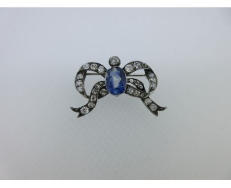 A sapphire and diamond ribbon bow brooch, the central oval cut light blue sapphire beneath an old European cut diamond surmou