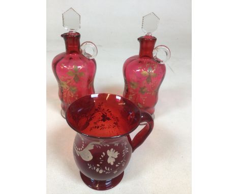 A pair of vintage cranberry glass small decanters decorated with gold flowers and a ruby glass jug with hand painted flowers.