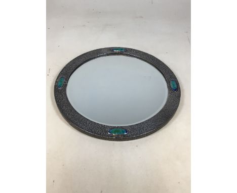 An Arts and Crafts circular pewter mirror. Frame mounted with four turquoise ceramic cabochons, centred with a bevelled edge 