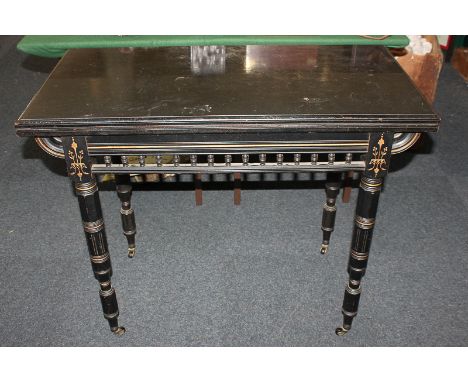 A Victorian ebonised rectangular card table with fold over green baise lined top, balustrade frieze with gilt detailing, on t