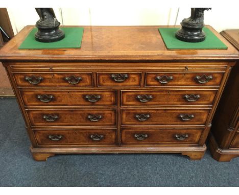 A George III style walnut and feather banded sideboard, with leather inset reverse breakfront top above an arrangement of nin