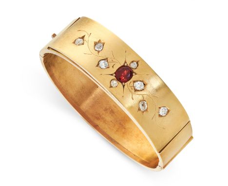 AN ANTIQUE GARNET AND DIAMOND BANGLE, CIRCA 1900 in yellow gold, the band set with a cushion cut garnet within engraved folia