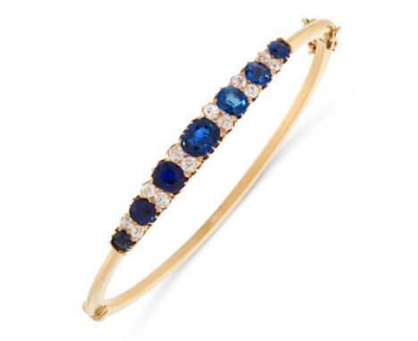 AN UNHEATED SAPPHIRE AND DIAMOND BANGLE in yellow gold set with a row of seven graduated cushion cut blue sapphires totalling