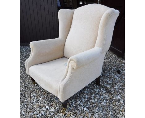 A modern Laura Ashley wing back arm chair in plain cream upholstery with ringed and turned front legs to brass caps and casto