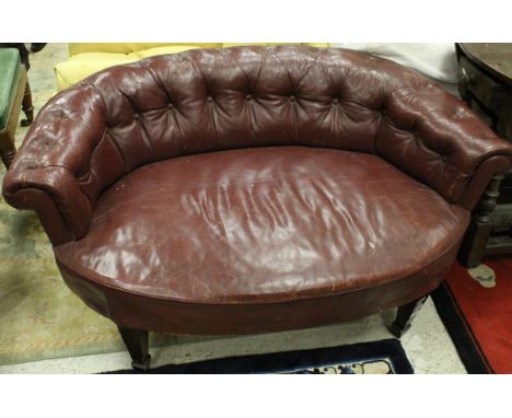 A circa 1900 red leather button back snuggler chair raised on square tapering legs to spade feet