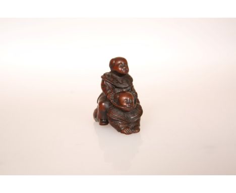 A JAPANESE WOOD NETSUKE, carved as two boys playing piggy back, signed. 45mm