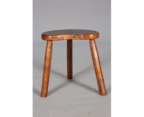 A FISHMAN OAK MILKING STOOL, CIRCA 1939, the adzed kidney shaped top raised on the splayed faceted legs, inscribed to undersi