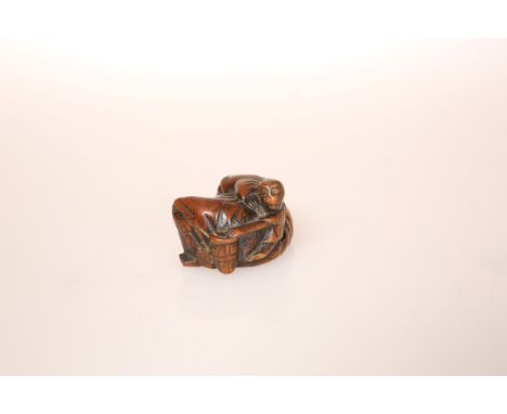 A JAPANESE WOOD NETSUKE OF A MONKEY TRAINER, possibly late 18th Century, the unsuspecting trainer lying asleep, his head rest