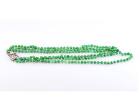 A JADEITE AND DIAMOND NECKLACE, formed of uniform jadeite beads each strung knotted into three graduating rows, on an elabora
