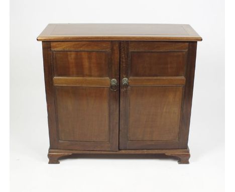 A 1920s mahogany floor standing cabinet the rectangular top above two panel cupboard doors with lion mask ring handles enclos