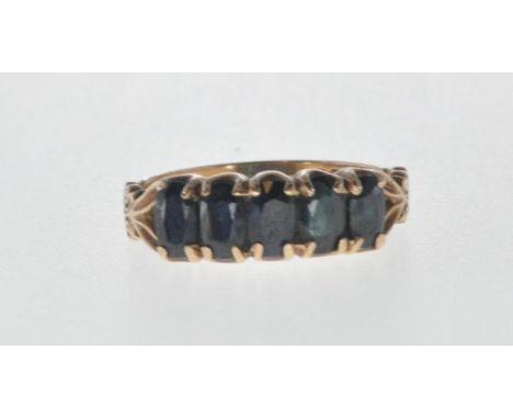 A hallmarked 9ct gold ring having a row of of five oval cut black stones, all within claw settings and the shoulders having e