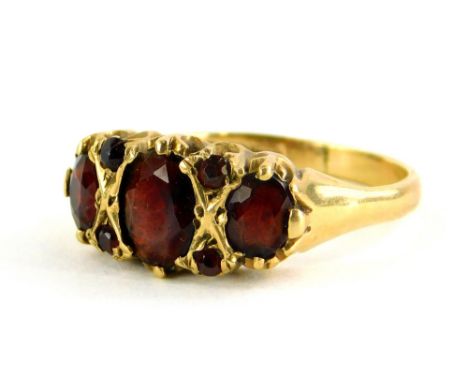 A 9ct gold garnet set dress ring, with three large oval cut garnets, dispersed with four tiny garnets, in a raised claw setti