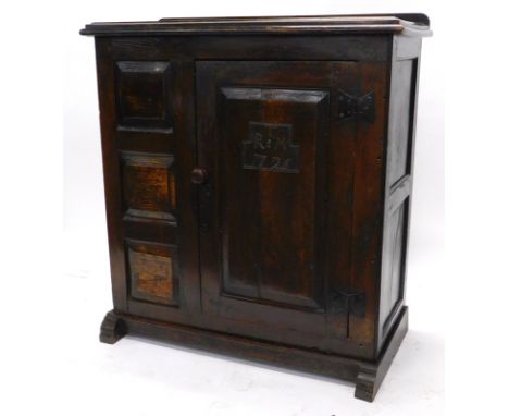 An early 18thC joined oak livery cupboard, the loose top with a moulded edge above a single panelled door bearing initials T 