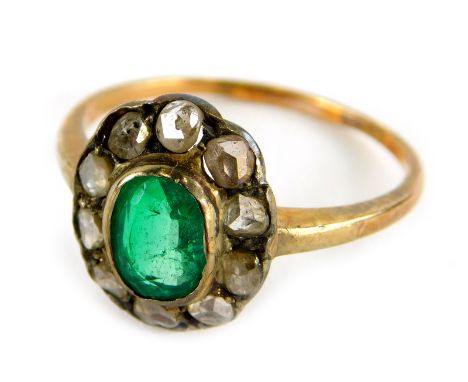 An emerald and diamond dress ring, in floral cluster with central oval cut emerald, surrounded by various diamonds chips, in 