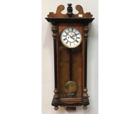 A walnut Vienna wall clock, the shaped pediment above a white enamel dial with Roman numerals denoting hours, flanked by turn