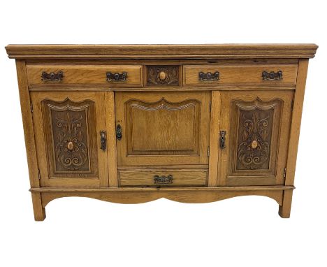 Edwardian light oak sideboard, two outer cupboards carved with scrolling motifs, enclosing smaller central cupboard above sin