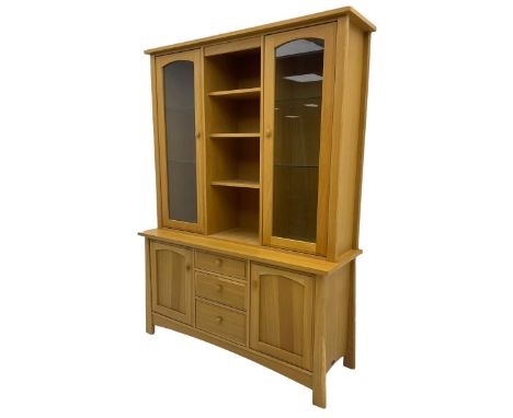 Light oak wall display cabinet, fitted with two glazed doors enclosing illuminated cupboards, above three drawers and two cup