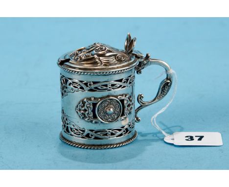 A GEORGE V CIRCULAR IRISH SILVER CELTIC INFLUENCE MUSTARD POT AND COVER, blue glass liner, decorated with dragons and interla