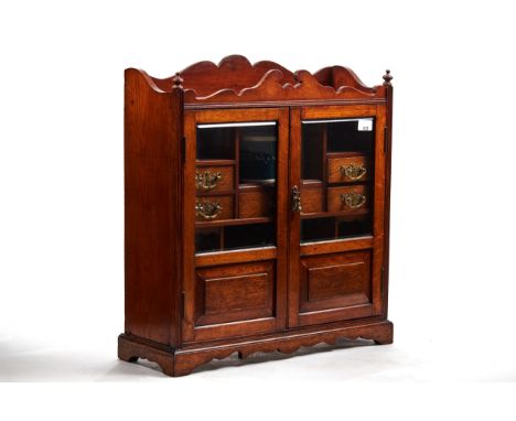 A LARGE EDWARDIAN OAK SMOKERS CABINET, twin glazed doors enclosing seven small drawers, shaped galleried back with finial cor