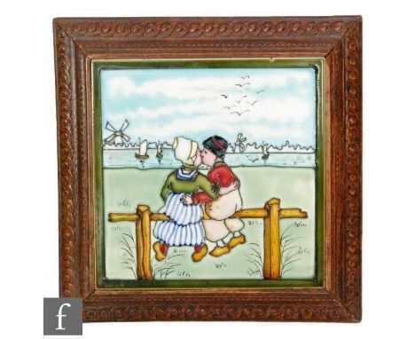 A framed 8in tile decorated with a tubelined Dutch scene with a lady and gentleman kissing whilst looking out to sea with a w