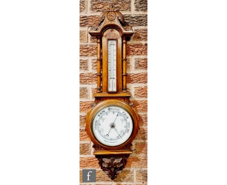 A Victorian carved oak aneroid barometer mounted with a thermometer above a white circular dial below a moulded scroll pedime
