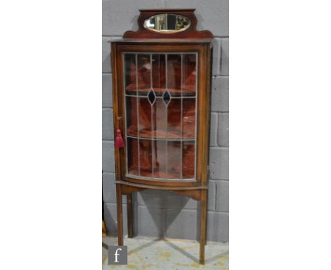 An Edwardian mahogany bow fronted display cabinet enclosed by a leaded light blue coloured glass panel door below a small ova