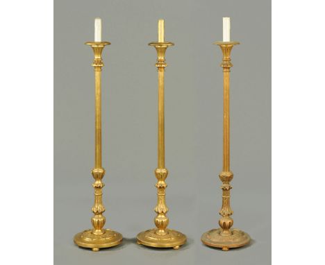 * A set of three carved and giltwood lamp standards, candle form tops, fluted columns and circular carved bases.  